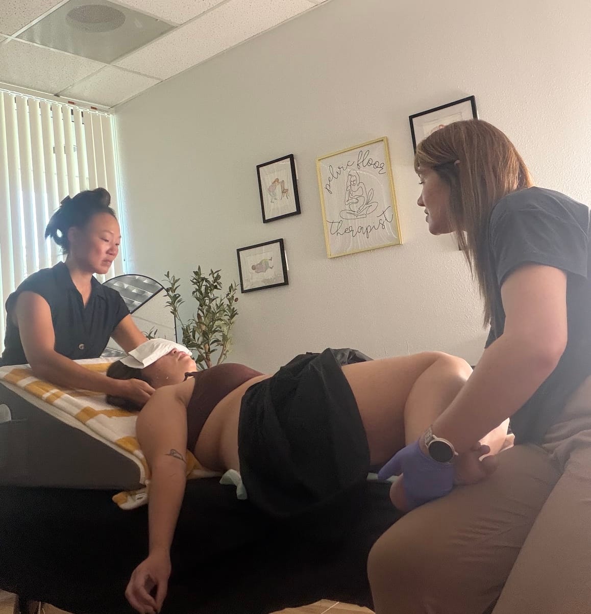A different angle of the co-treatment. Nina performs facial and jaw work at the patient's head while Ashlee supports the lower body during a Reconnection Session at AG Physical Therapy.