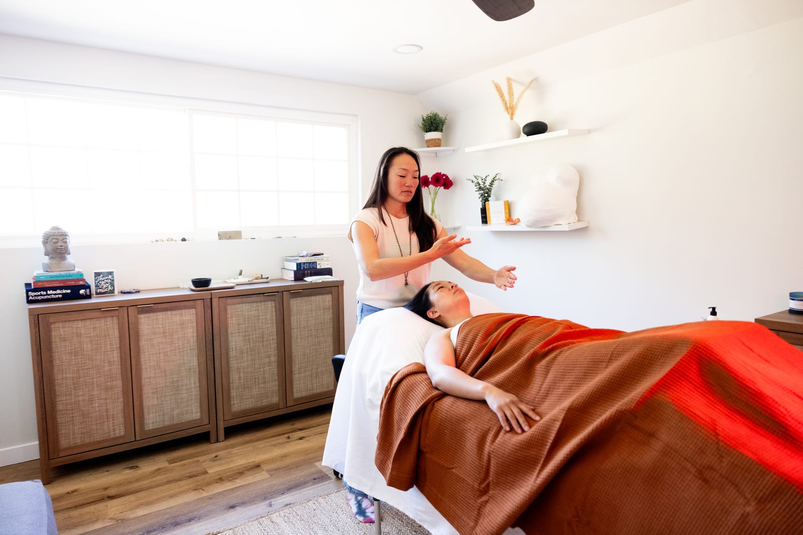Nina treats a patient resting under a terracotta blanket in her sunlit Poway clinic.