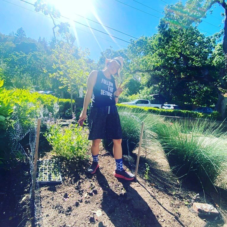 Nina Jung standing in a sunlit garden bed in a 'Follow the Detour' tank top.