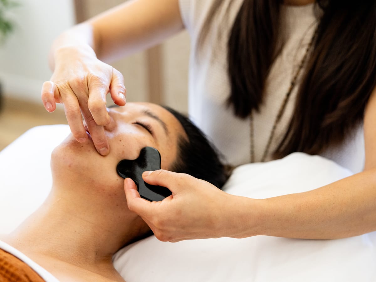 Facial gua sha performed with a smooth tool along a patient's cheek and jaw.